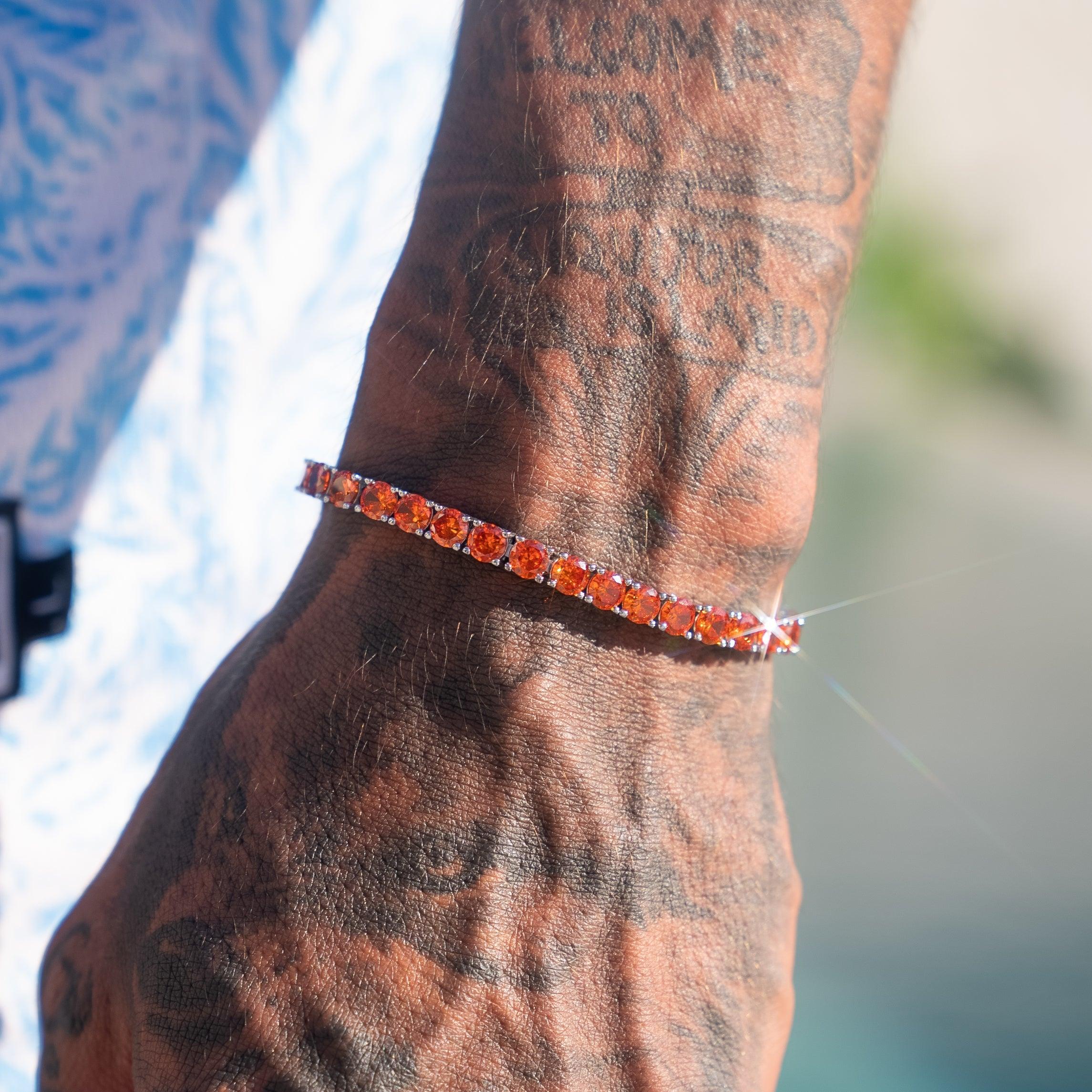 5mm red ruby tennis bracelet on tattooed wrist, sparkling in sunlight.